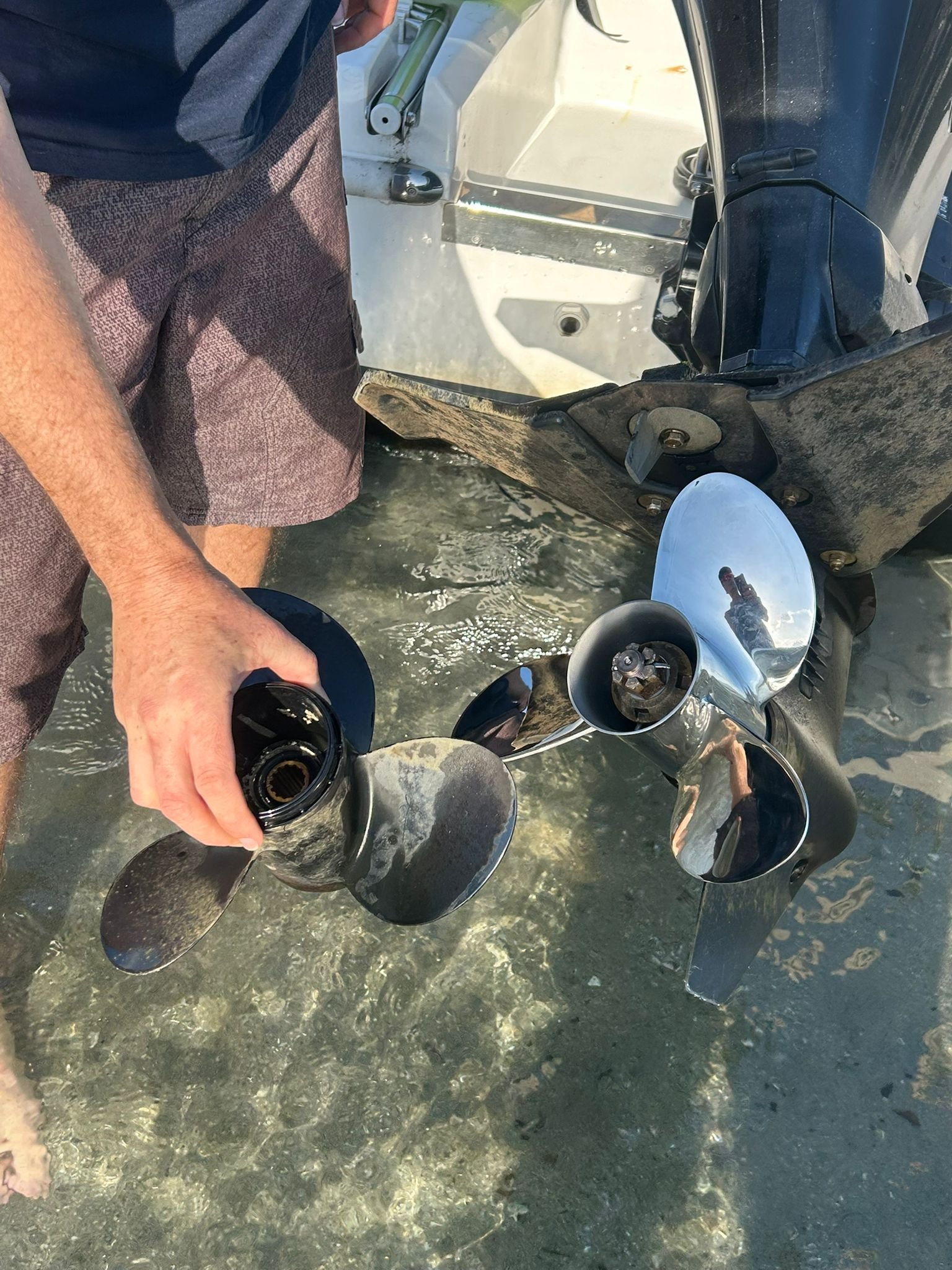 Customer handling a polished three-blade stainless steel propeller beside a Suzuki outboard
